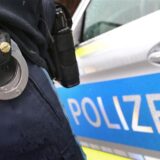 Ein Polizist mit Handschellen und einer Pistole am Gürtel steht vor einem Streifenwagen.