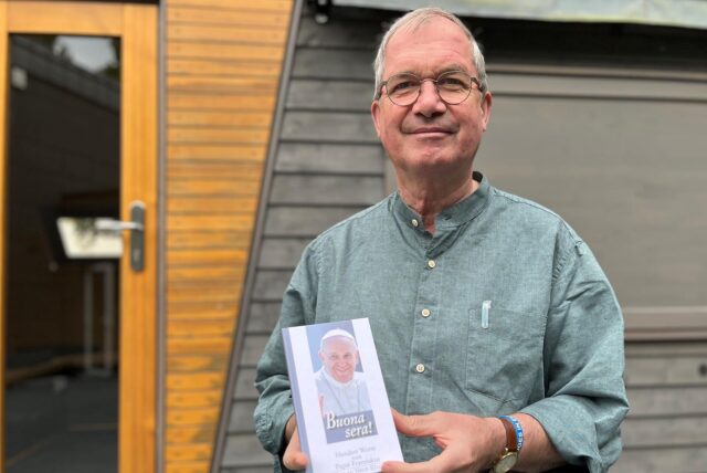 Meinolf Wacker steht in seinem Garten vor einem sogenannten Tiny House. In der Hand hält der Pastor ein Buch mit Texten des früheren Papstes Franziskus.
