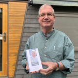 Meinolf Wacker steht in seinem Garten vor einem sogenannten Tiny House. In der Hand hält der Pastor ein Buch mit Texten des früheren Papstes Franziskus.