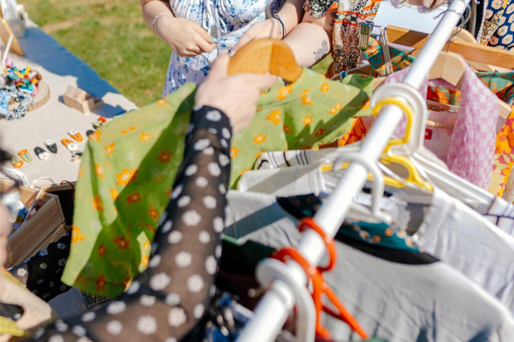 Auf einem Trödelmarkt-Stand liegen verschiedenste Accessoires - daneben steht eine Kleiderstange mit bunten Blusen, T-Shirts und weiteren gebrauchten Kleidungsstücken. Auf einem Trödelmarkt-Stand liegen verschiedenste Accessoires - daneben steht eine Kleiderstange mit bunten Blusen, T-Shirts und weiteren gebrauchten Kleidungsstücken.