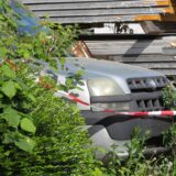 Flatterband und wucherndes Grün umschlingen ein abgestelltes Auto, das auf dem Gelände von Strothmann Automobile in Unna auf die Zerlegung und Verwertung wartet.