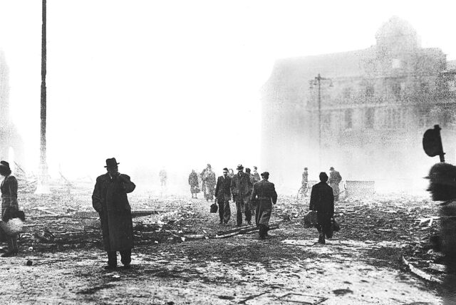 Menschen gehen durch Trümmer und Rauch auf dem Hansaplatz nach einem Bombenangriff.