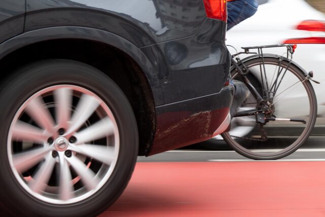 Ein Fahrrad fährt neben einem Auto her.