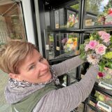 Maraike von Eynern bestückt den Blumenautomaten bei Scharrenbach in Kamen. Sie lächelt in die Kamera, die Hände an einem Strauß.
