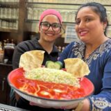 Chefin Navnit Kaur und ihre Nichte Tarandeep Kaur halten im Restaurant Flamingo am Zoo Dortmund einen Teller mit einem indischen Gericht in die Kamera.
