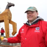 Geschäftsführer Thomas Wiese stößt mit dem Künstler an, der die große Pferdeskulptur auf dem Außengelände des Reitsportzentrums Massener Heide angefertigt hat. Im Hintergrund steht die Figur selbst.