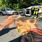 Zwei Autos stehen voreinander, Feuerwehrleute sind zu sehen. Die beiden Fahrzeuge sind zusammengestoßen.