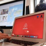 Auf einem Laptop und einem Bildschirm im Büro der Airbnb Germany GmbH in der Neuen Schönhauser Straße sind das Logo des Unternehmens und eine Auswahl von Unterkünften zu sehen. (Archivbild)