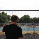 Ein junger Mann beobachtet die Baustelle zum neuen Sesekebad in Kamen durch einen Bauzaun hindurch.