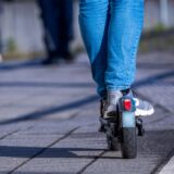 Eine Person fährt mit einem E-Scooter. Nur ein Teil der Hose und die Schuhe auf dem Fahrzeug sind zu sehen.