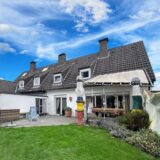 Die Doppelhaushälfte verfügt über einen Garten mit Wiese und Beet sowie einer Terrasse auf der ein gestreifter Liegestuhl steht.