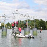 Gäste klettern auf dem „Aqua-Climb“. Eine Person fällt vom Kletter-Parcours in den Ternscher See.