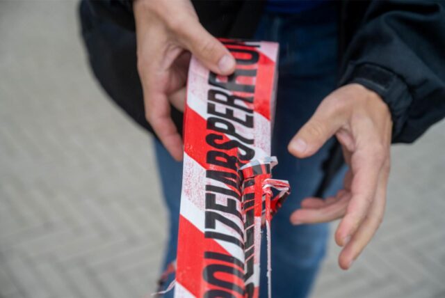 Ein Mann rollt weiß-rotes Absperrband mit der Aufschrift „Polizeiabsperrung“ ab