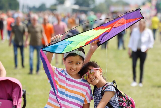 Zwei Mädchen stehen mit einem Drachen auf dem Gelände des Drachenfestivals Kamen Kite