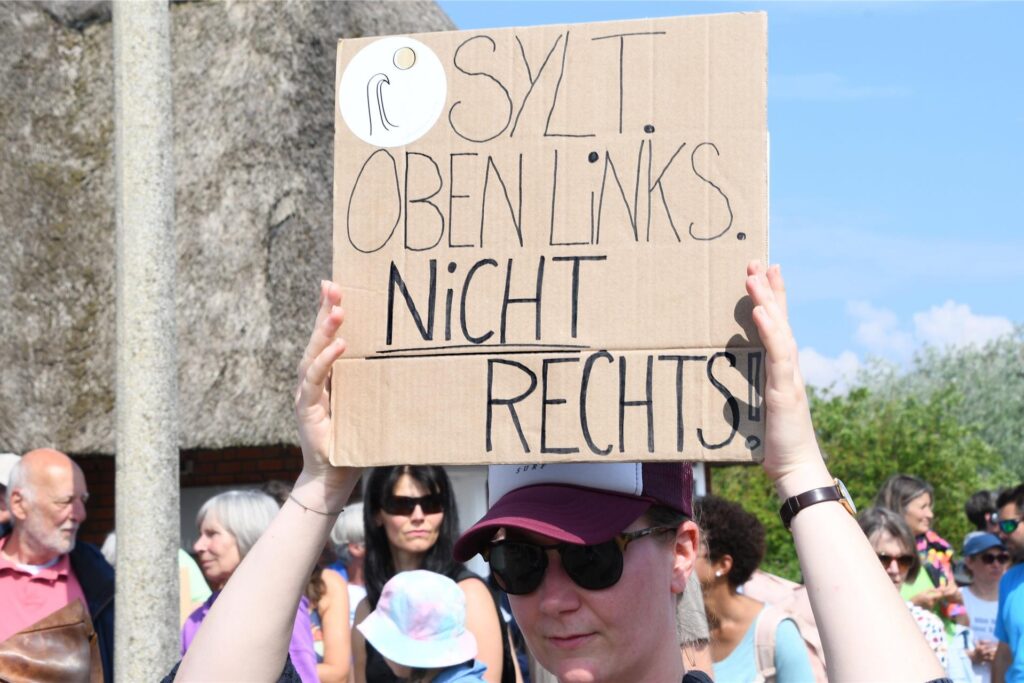 „Sylt oben links nicht rechts“ steht auf einem Plakat, dass eine Frau bei einer Mahnwache am 26.05.2024 auf Sylt in der Hand hält.