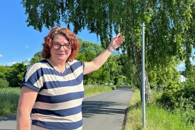 Kirsten Braß aus Lünern steht an der Kuhstraße an einem Schildermast, an dem kein Schild angebracht ist. Eigentlich sollte dort eine Tafel Tempo 50 vermelden.