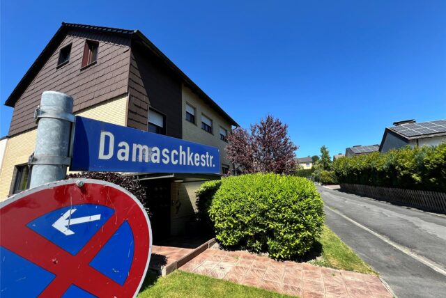 Ein Polizist mit Handschellen und einer Pistole am Gürtel steht vor einem Streifenwagen.
