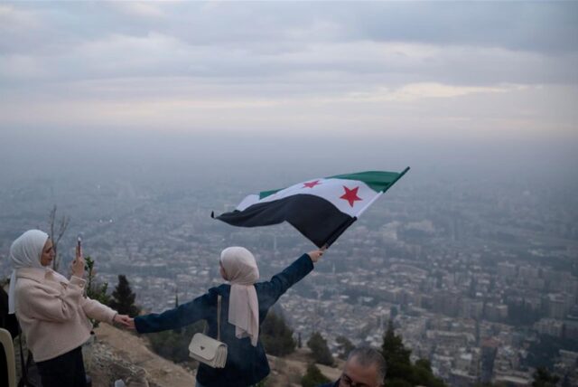 Eine junge Frau posiert für ein Foto mit einer Flagge der syrischen Opposition an einem Aussichtspunkt auf dem Berg Qasiyun oberhalb der Stadt Damaskus.