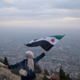 Eine junge Frau posiert für ein Foto mit einer Flagge der syrischen Opposition an einem Aussichtspunkt auf dem Berg Qasiyun oberhalb der Stadt Damaskus.