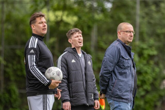 Lorenz Wagener (M.) steht neben zwei Männern und ärgert sich.