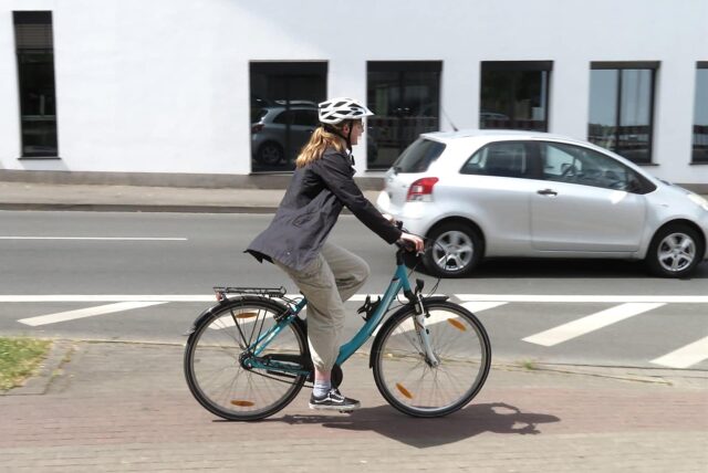 Eine junge Frau fährt mit ihrem Fahrrad vom freigegebenen Gehweg aus auf den Ostring zu. Dort muss sie sich in den fließenden Autoverkehr einordnen.