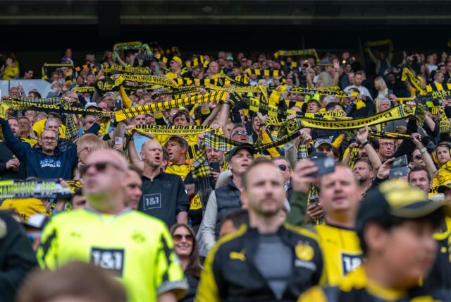 BVB-Fans stehen auf der Tribüne und halten ihren Schal in die Höhe.