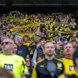 BVB-Fans stehen auf der Tribüne und halten ihren Schal in die Höhe.