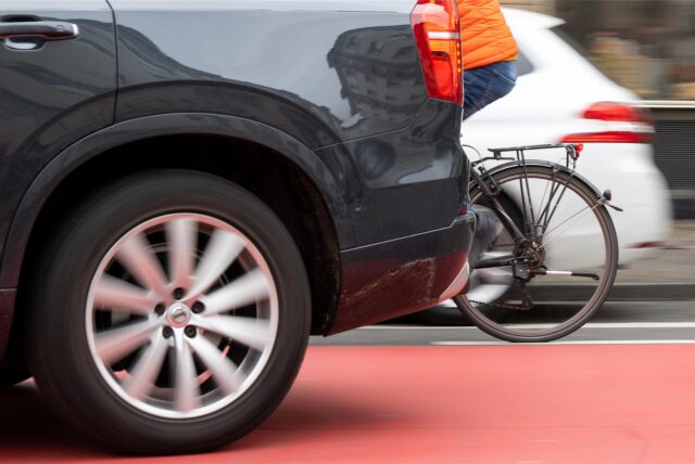 Ein Fahrradfahrer fährt zwischen zwei fahrenden Autos her.