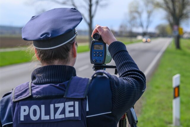 Eine Polizistin misst mit einem Lasergerät die Geschwindigkeit von vorbeifahrenden Autos. Auf dem Display des Geräts sind 74 km/h zu erkennen.