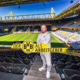 Chmielewski steht zwischen den Zuschauerrängen im Stadion, im Hintergrund sieht man das Spielfeld