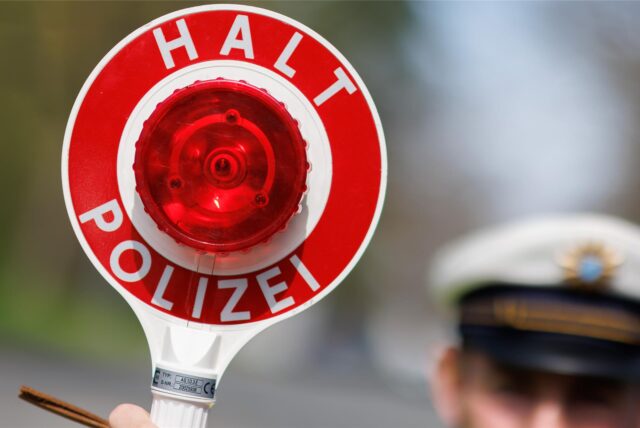 Ein Polizist hält eine rote Verkehrskelle in die Höhe.