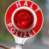 Ein Polizist hält eine rote Verkehrskelle in die Höhe.