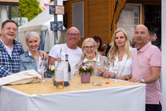 Drei Frauen und drei Männer stehen bei der Festa Italiana 2023 in Unna an einem Stehtisch und trinken Weißwein.
