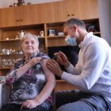 Ein Arzt gibt einer Patientin in ihrem Wohnzimmer eine Spritze.
