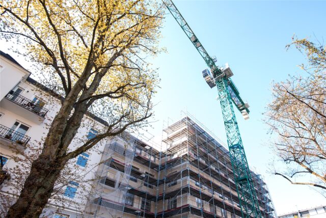 Ein Baukran steht neben einem Neubau, der mit Gerüsten versehen ist