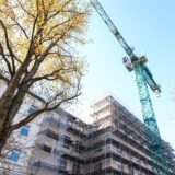 Ein Baukran steht neben einem Neubau, der mit Gerüsten versehen ist
