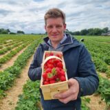 Christoph Schulte streckt einen Korb Erdbeeren in die Kamera.