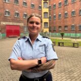 Isabelle Lymers verschränkt die Arme im Hof der Justizvollzugsanstalt Dortmund, wo sie eine Ausbildung zur Justizvollzugsbeamtin macht.