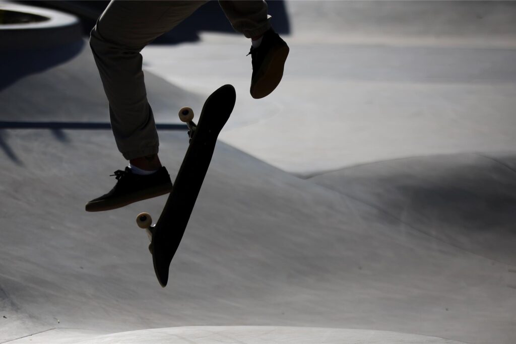 Ein Skateboarder ist in einem Skatepark in der Luft zu sehen. Der Skateboarder trägt helle Hosen und dunkle Schuhe mit hellen Sohlen.