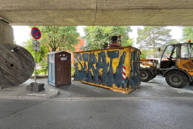 Unter der B233-Brücke an der Bahnhofstraße in Kamen stehen unter anderem ein Dixi-Klo, ein Baucontainer und ein Baustellenfahrzeug.