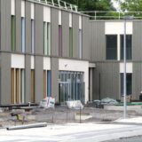 Die Außenfassade der neuen Schule am Hertinger Tor ist geprägt von einer grauen Holzlattung, weißen Putzflächen und bunt gestrichenen Fensterleibungen.