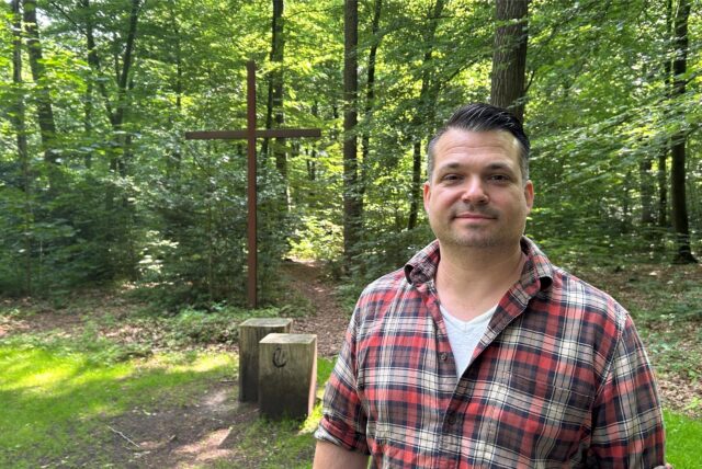 Förster Maximilian Brauer steht am großen Andachtsplatz des Ruheforsts. Hinter ihm ist ein großes, braunes Kreuz zu sehen.