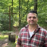 Förster Maximilian Brauer steht am großen Andachtsplatz des Ruheforsts. Hinter ihm ist ein großes, braunes Kreuz zu sehen.