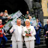 Ralf Wiethaup und Doris Hübecker stehen nach ihrer Trauung vor dem Rathaus in Recklinghausen, im Hintergrund gratulieren die Kollegen der Recklinghäuser Zeitung mit Zeitungsstöcken und Blumen