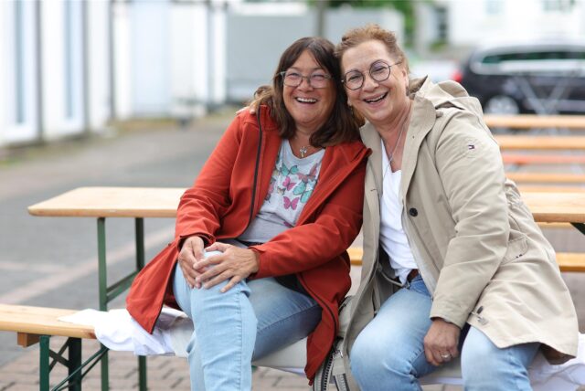 Zwei Frauen sitzen lachend auf einer Bank.
