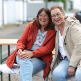 Zwei Frauen sitzen lachend auf einer Bank.