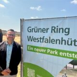 Grünflächenamts-Leiter Heike Just neben einem Transparent zum Bau des „Grünen Rings“. „Ein neuer Park entsteht“, steht darauf.