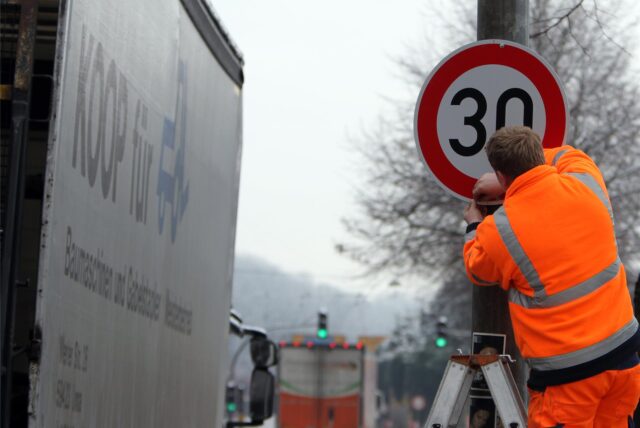 Ein Arbeiten mit Warnweste montiert ein Tempo-30-Schild.