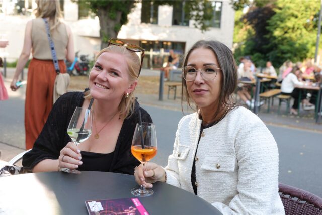 Zwei Frauen sitzen in der Lüner Innenstadt an einem Tisch und trinken aus Weingläsern.