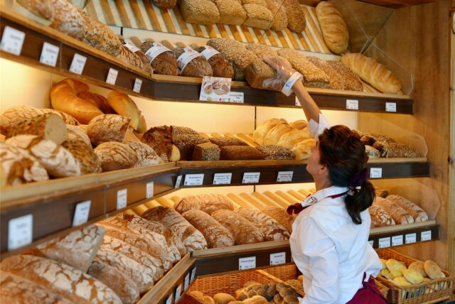Eine Verkäuferin beim Bäcker greift in ein Brot-Regal.